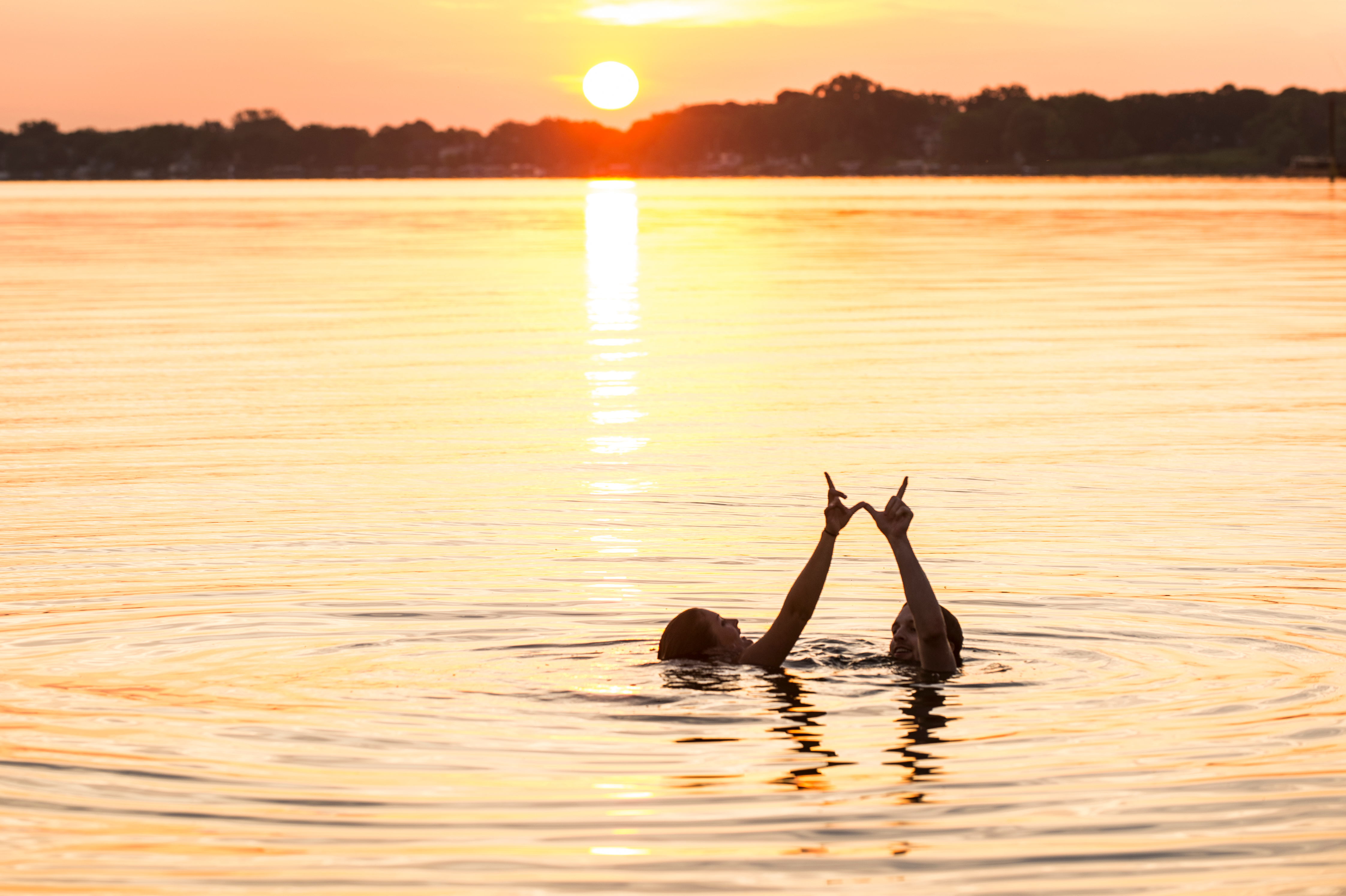 Having stayed up all night, undergraduates Loran Zweifelhofer and Willis Perley form a W hand sign as they greet the morning sunrise over Lake Mendota with a swim from the Goodspeed Family Pier near the Memorial Union Terrace at the University of Wisconsin-Madison on June 19, 2015. The two friends met during their freshman year and are now seniors. (Photo by Jeff Miller/UW-Madison)
