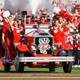 Members of UW Spirit Squad ride the Bucky Wagon onto the field at Camp Randall Stadium before the homecoming football game. The driver of Bucky Wagon is Glenn Bower, the manager of the wagon and automotive faculty adviser for UW-Madison's College of Engineering.