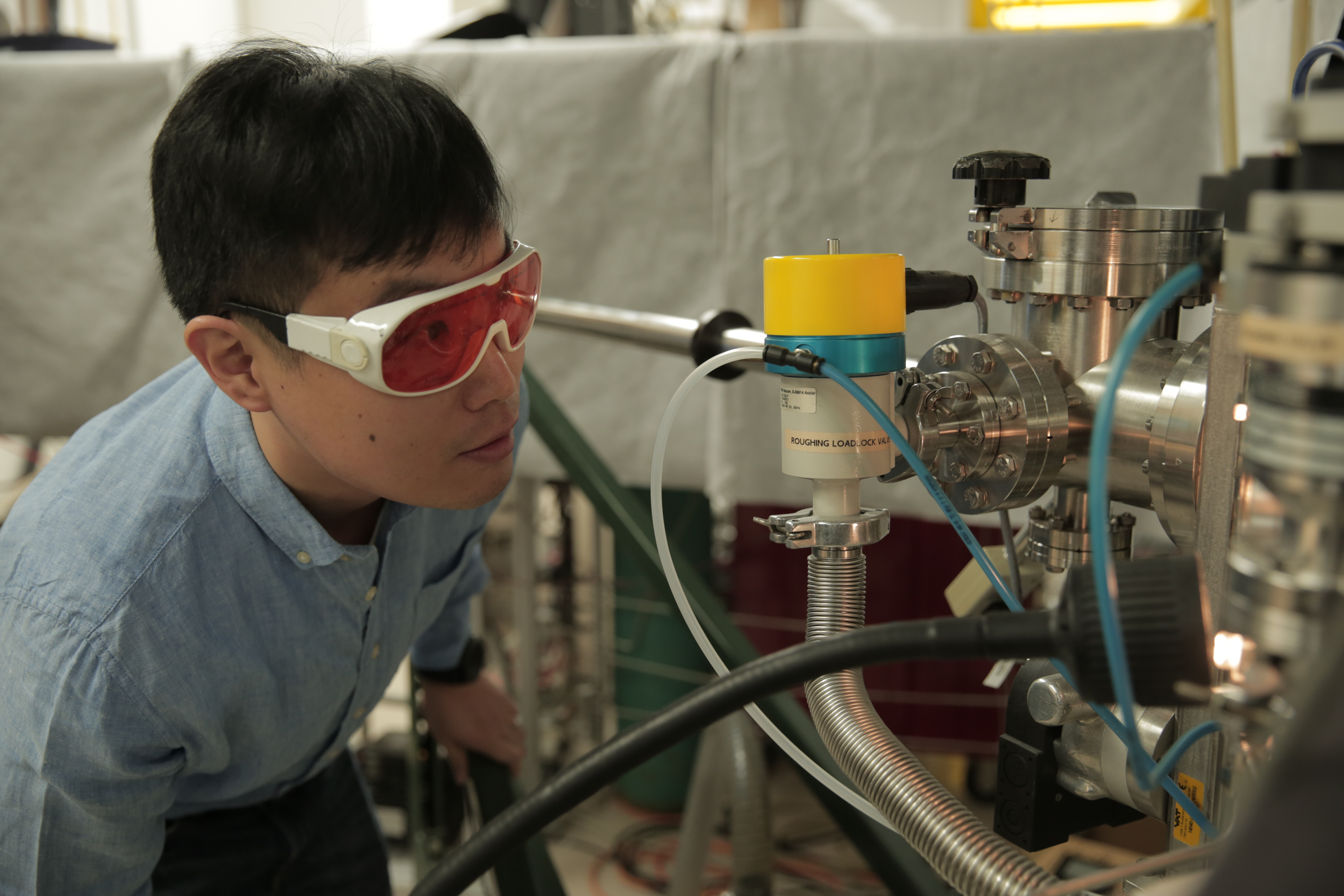 Materials science and engineering postdoctoral researcher Hyungwoo Lee looks inside a thin film deposition system during oxide thin film structure growth. 