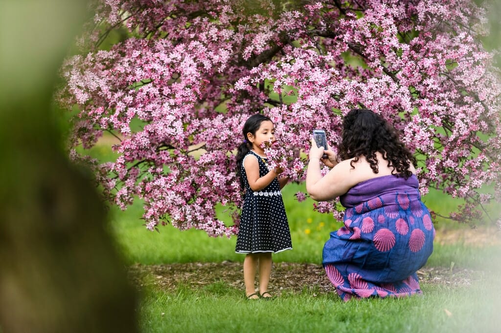 Photo: Woman taking photo of young girl in front of tree