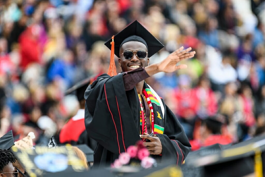 Photo of Charles Fatunbi, graduating with a bachelor's degree in industrial engineering, waving to the crowd.